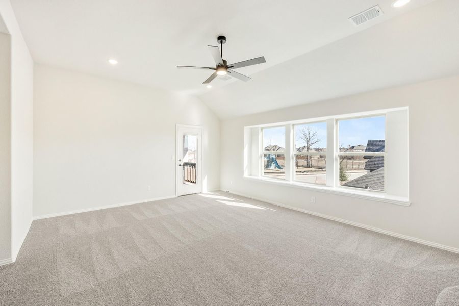 Empty room with vaulted ceiling, ceiling fan, carpet flooring, and large windows overlooking a neighborhood