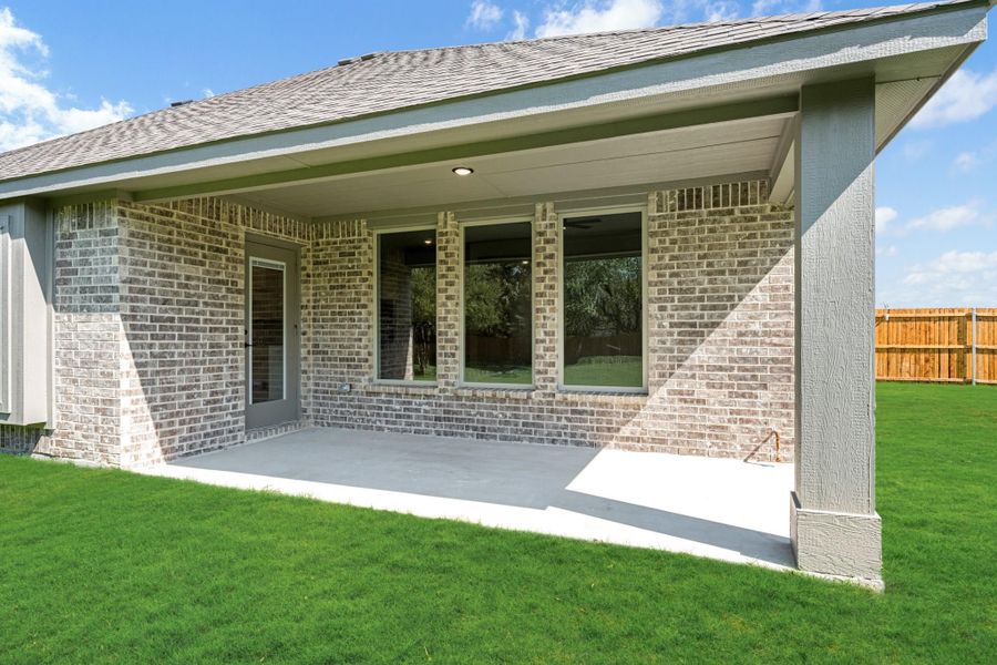 Covered back patio with concrete slab, brick exterior, and green lawn with wood privacy fence