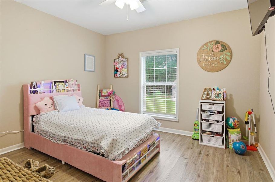 Spacious room featuring wood-finish flooring, a ceiling fan with light, and a window with blinds