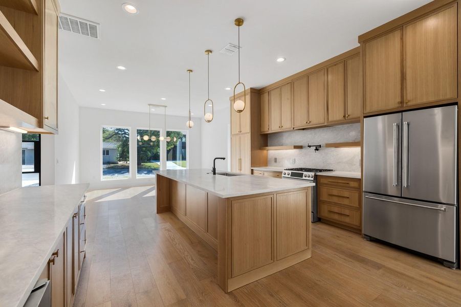 Kitchen with open shelves, appliances with stainless steel finishes, light wood finished floors, pendant lighting, and light stone counters Kitchen with open shelves, appliances with stainless steel finishes, light wood finished floors, pendant lighting, and light stone counters