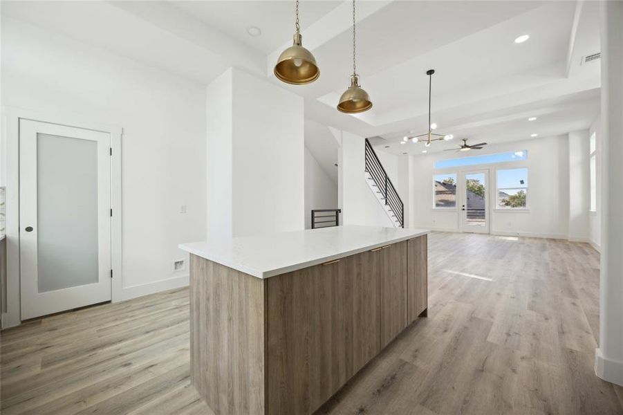 Bright and spacious modern kitchen and living area with high ceilings, featuring a large kitchen island, contemporary light fixtures, and a view of the outside through patio doors. Enjoy a clean, minimalist aesthetic with ample natural light!