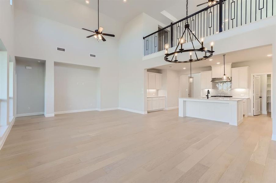 Unfurnished living room featuring high vaulted ceiling, light hardwood / wood-style floors, ceiling fan with notable chandelier, and sink