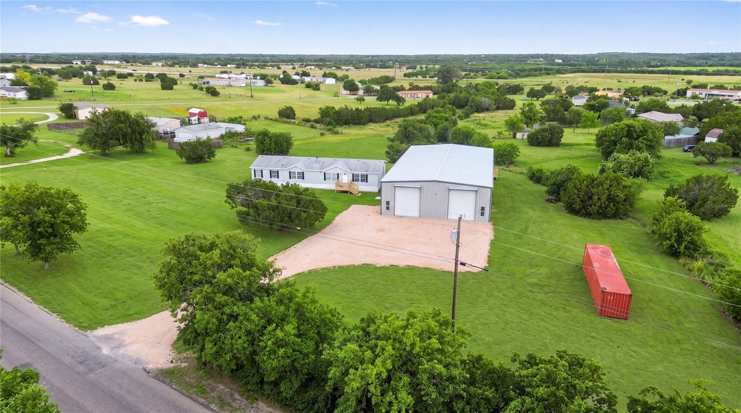 An expansive rural property features a large detached metal workshop on a grassy lawn.