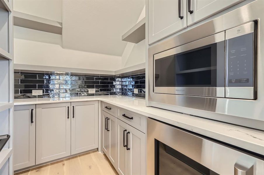 Kitchen with wine cooler, light hardwood / wood-style flooring, backsplash, white cabinetry, and stainless steel microwave