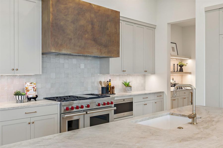 Kitchen with light stone counters, range with two ovens, tasteful backsplash, and a sink Kitchen with light stone counters, range with two ovens, tasteful backsplash, and a sink