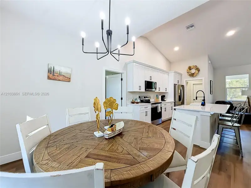 Open-concept kitchen featuring white shaker cabinetry, stainless steel appliances, a central island with a solid-surface countertop, and a contemporary six-arm chandelier