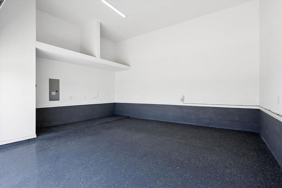 Spacious garage featuring a durable epoxy floor finish, overhead linear lighting, built-in shelving, an electrical service panel, and a water spigot