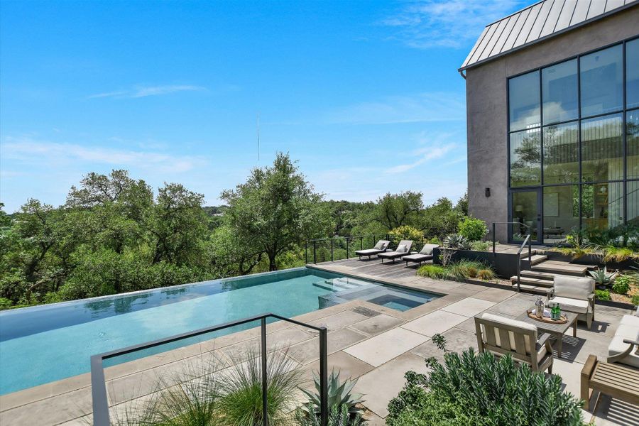 Infinity-edge swimming pool with integrated spa, expansive concrete patio, multi-level landscaping, and a modern exterior with floor-to-ceiling windows