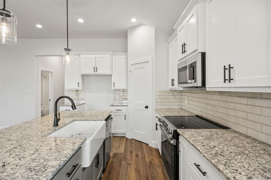 Kitchen featuring stainless steel appliances, light stone counters, white cabinets, dark wood-style flooring, and backsplash