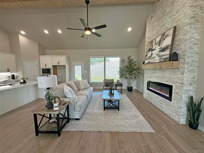 Living area featuring light wood-style floors, high vaulted ceiling, recessed lighting, a ceiling fan, and a fireplace Living area featuring light wood-style floors, high vaulted ceiling, recessed lighting, a ceiling fan, and a fireplace