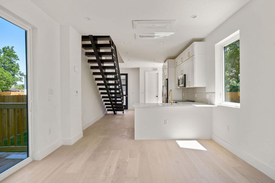 Kitchen featuring stainless steel appliances, white cabinets, light wood-type flooring, and light countertops