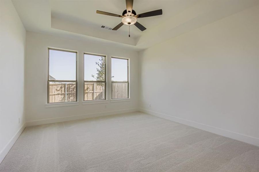 Empty room with a raised ceiling, light colored carpet, and ceiling fan Empty room with a raised ceiling, light colored carpet, and ceiling fan