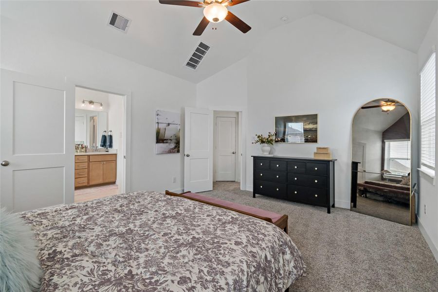 Spacious master bedroom featuring vaulted ceilings, a cozy fan, and abundant natural light from large windows. The room connects to a stylish ensuite bathroom. Spacious master bedroom featuring vaulted ceilings, a cozy fan, and abundant natural light from large windows. The room connects to a stylish ensuite bathroom.