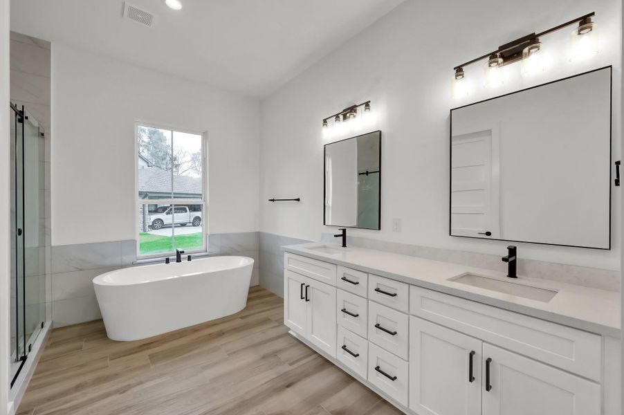 Luxurious primary bathroom featuring a freestanding soaking tub, oversized walk-in shower, dual vanities with quartz countertops, and designer lighting.
