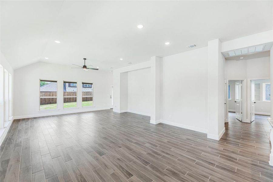 Open living room with vaulted ceiling, ceiling fan, wood-look floors, and large windows overlooking backyard Open living room with vaulted ceiling, ceiling fan, wood-look floors, and large windows overlooking backyard