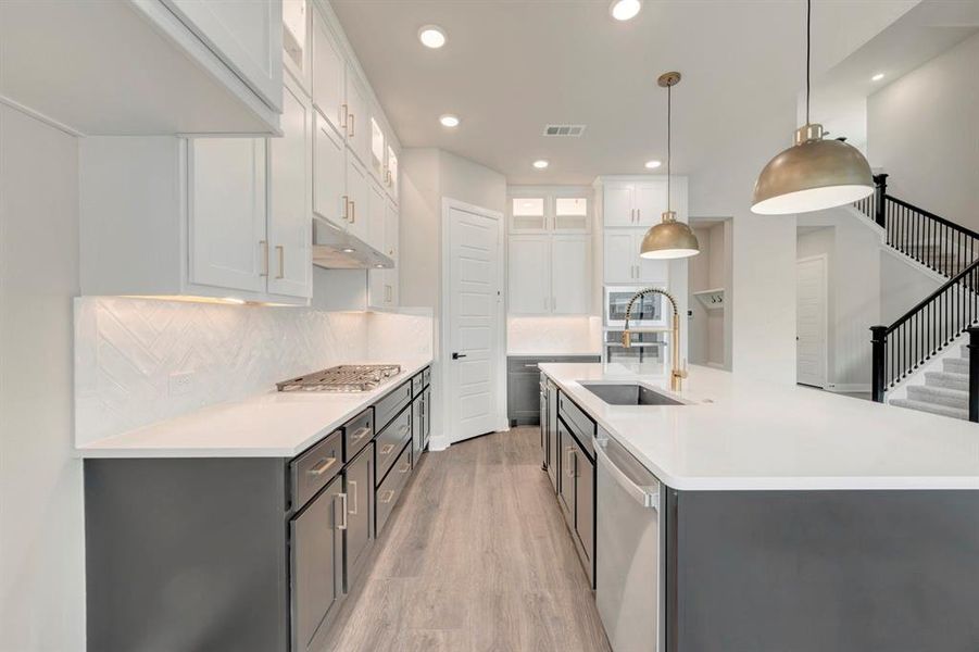 Kitchen featuring glass fronted cabinets, two tone cabinetry, backsplash, light wood-style flooring, and stainless steel appliances