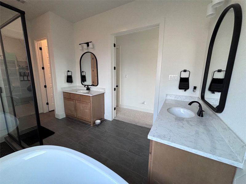The modern master bathroom featuring dual vanities with marble countertops, sleek black fixtures, and oval mirrors.