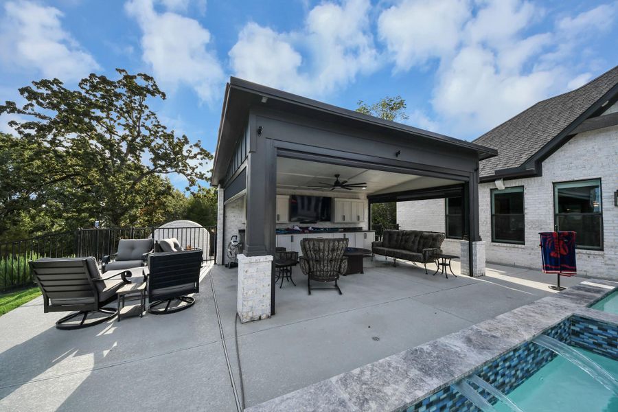 Stunning outdoor living space featuring a covered patio with comfortable seating, a ceiling fan, and a built-in entertainment area, perfect for relaxation and entertaining by the pool.
