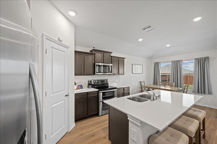 Kitchen with appliances with stainless steel finishes, dark brown cabinets, a kitchen island with sink, light wood-type flooring, and a breakfast bar area Kitchen with appliances with stainless steel finishes, dark brown cabinets, a kitchen island with sink, light wood-type flooring, and a breakfast bar area
