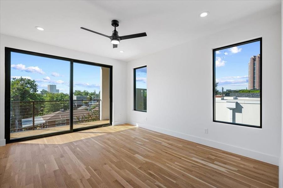 Primary bedroom featuring light wood finished floors, healthy amount of natural light, ceiling fan, and recessed lighting. Bedrom & balcony features downtown views. Primary bedroom featuring light wood finished floors, healthy amount of natural light, ceiling fan, and recessed lighting. Bedrom & balcony features downtown views.