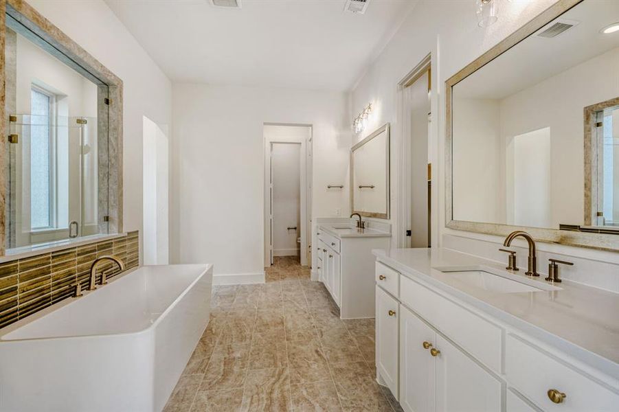Full bathroom featuring two vanities, a stall shower, a soaking tub, and plenty of natural light
