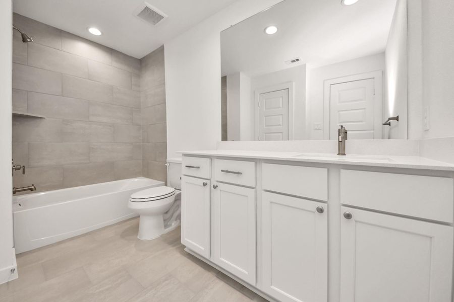 Secondary bath features tile flooring, bath/shower combo with tile surround, light stained wood cabinets, beautiful light countertop.