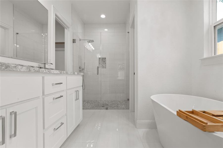 Bright bathroom featuring a freestanding soaking tub, a frameless glass shower enclosure with a rain shower head, and a double vanity with a stone countertop