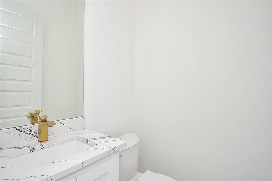 Elegant and modern, this powder room features a sleek quartz vanity with bold veining, complemented by luxurious gold fixtures. Bright and airy, its timeless design exudes sophistication and style.