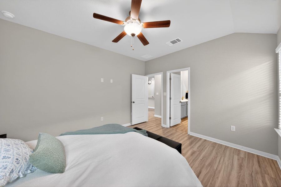 Bedroom featuring a ceiling fan, light wood finished floors, lofted ceiling, and ensuite bath