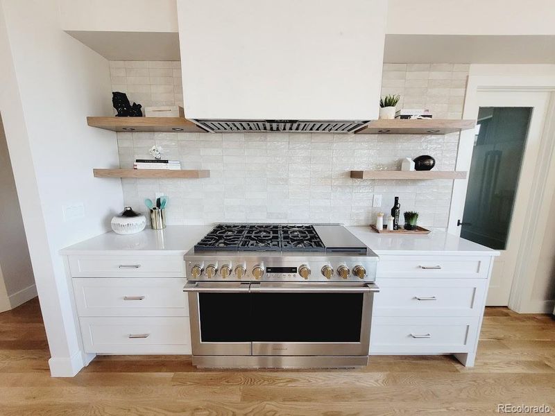 Chefs kitchen with 6 burner Monogram gas range with griddle, plaster range hood, designer tile, quartz countertops