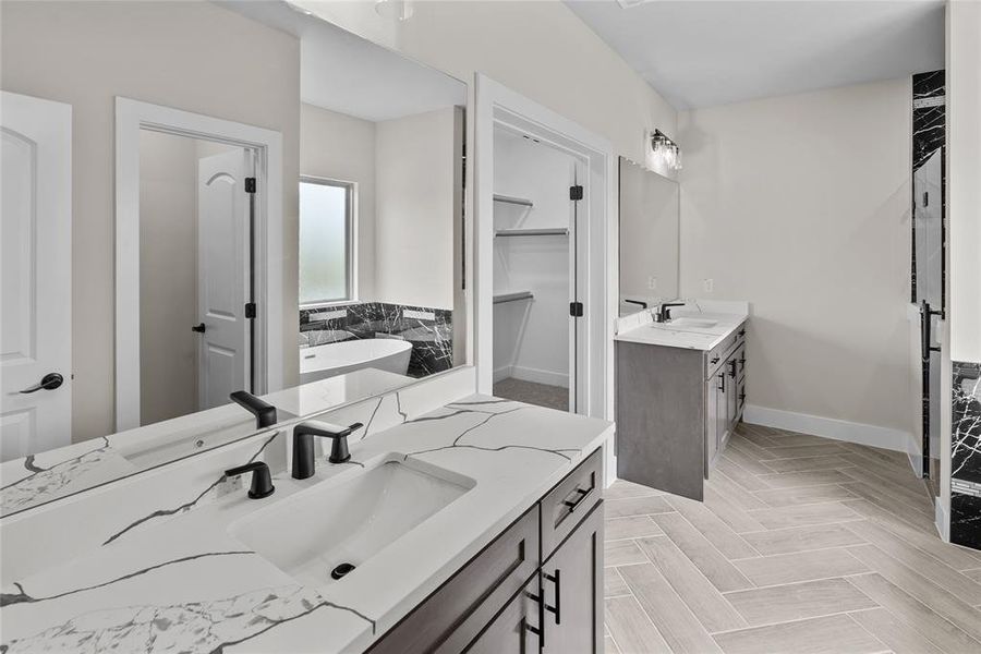 Bathroom with two vanities, baseboards, a freestanding bath, and a spacious closet