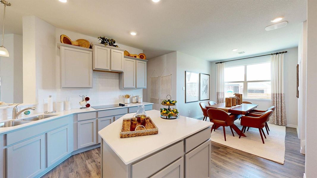 Kitchen featuring light wood-style flooring, a kitchen island, decorative light fixtures, black electric stovetop, and light stone countertops Kitchen featuring light wood-style flooring, a kitchen island, decorative light fixtures, black electric stovetop, and light stone countertops