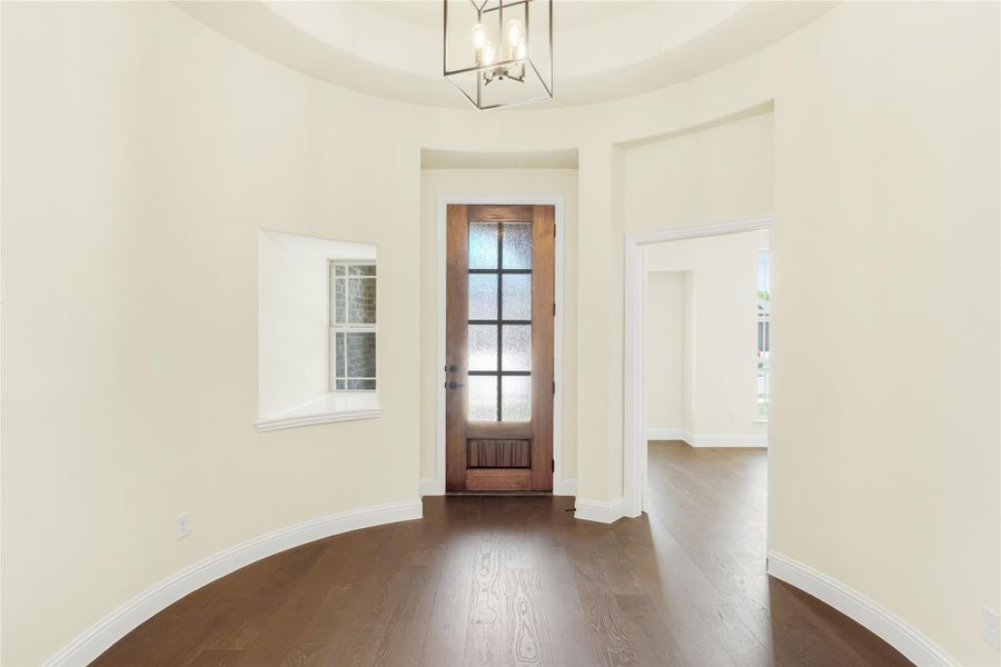 Rounded foyer with dark hardwood floors, wood front door with glass panels, and modern chandelier overhead Rounded foyer with dark hardwood floors, wood front door with glass panels, and modern chandelier overhead