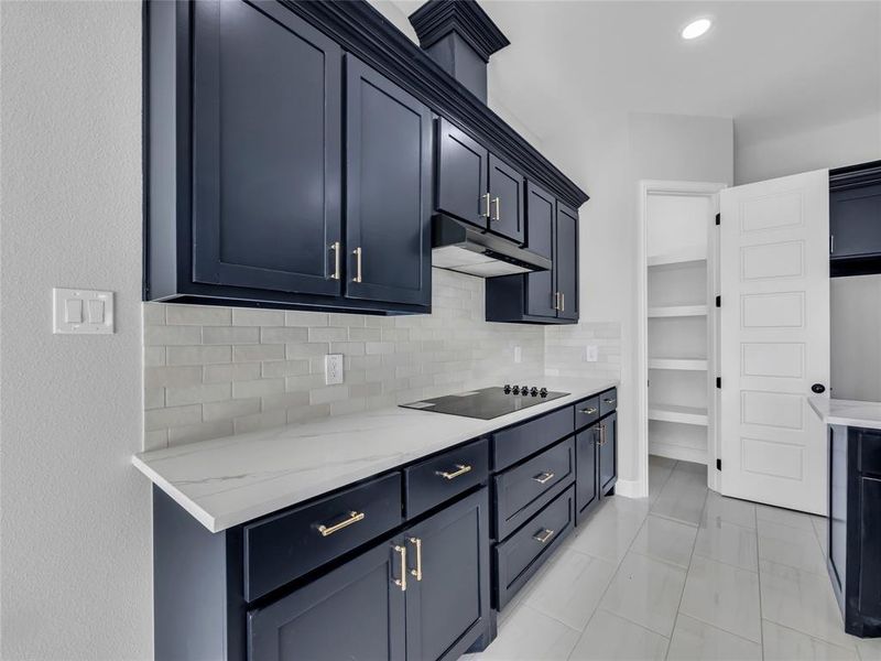 Kitchen featuring light stone countertops, backsplash, under cabinet range hood, and black electric stovetop Kitchen featuring light stone countertops, backsplash, under cabinet range hood, and black electric stovetop