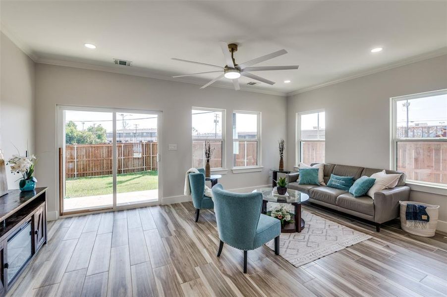 Living room with ceiling fan, a healthy amount of sunlight, ornamental molding, and light wood-type flooring