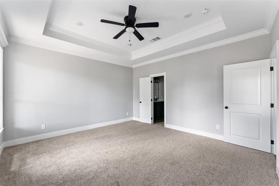 Unfurnished bedroom with a raised ceiling, ornamental molding, carpet flooring, a ceiling fan, and ensuite bathroom