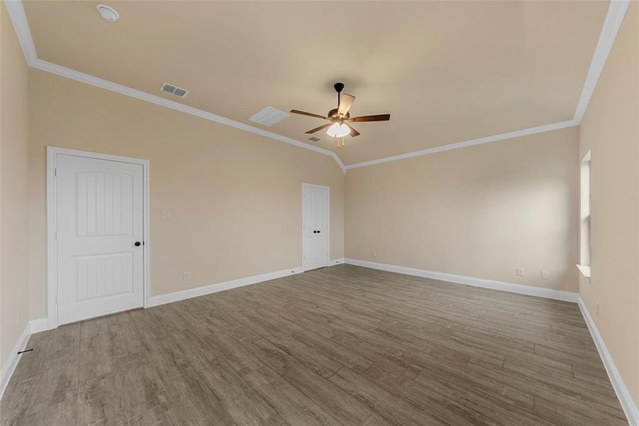 Spare room with a ceiling fan, crown molding, wood finished floors, baseboards, and lofted ceiling