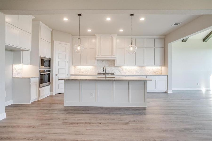 Kitchen with light wood-type flooring, an island with sink, decorative light fixtures, white cabinetry, and stainless steel appliances