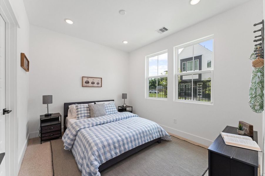 Located on the first floor for added accessibility and privacy, this secondary bedroom offers both comfort and charm with peaceful views of the community courtyard just beyond its large windows. Natural light fills the space, highlighting its warm tones and versatile layout—ideal for guests, in-laws, or a private home office. The ensuite bathroom features modern fixtures, a sleek vanity, and a tub-shower combo, creating a self-contained retreat that blends privacy, convenience, and a touch of greenery.