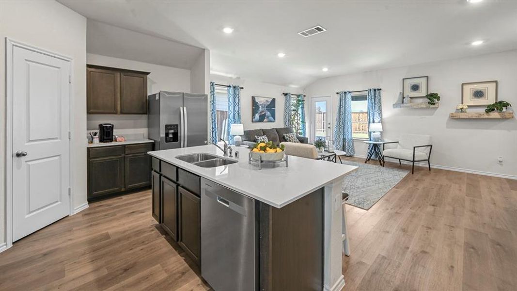 Kitchen featuring open floor plan, stainless steel appliances, dark wood finish cabinets, an island with sink, and recessed lighting