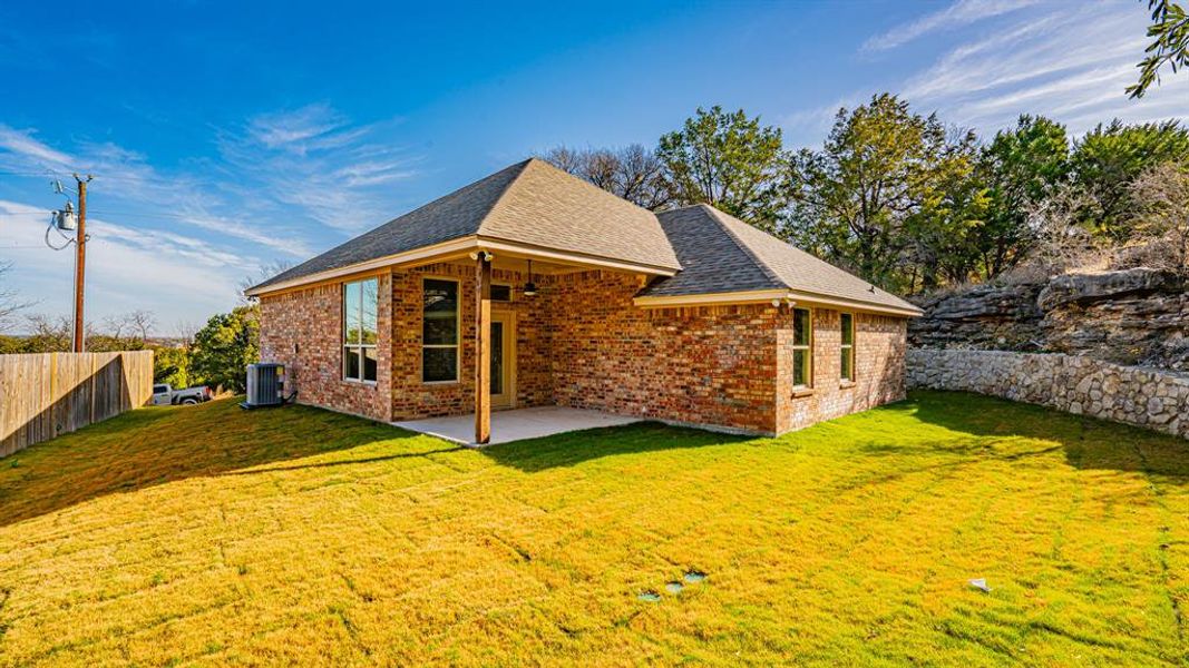 Rear view of property featuring brick siding, a patio, and a shingled roof
