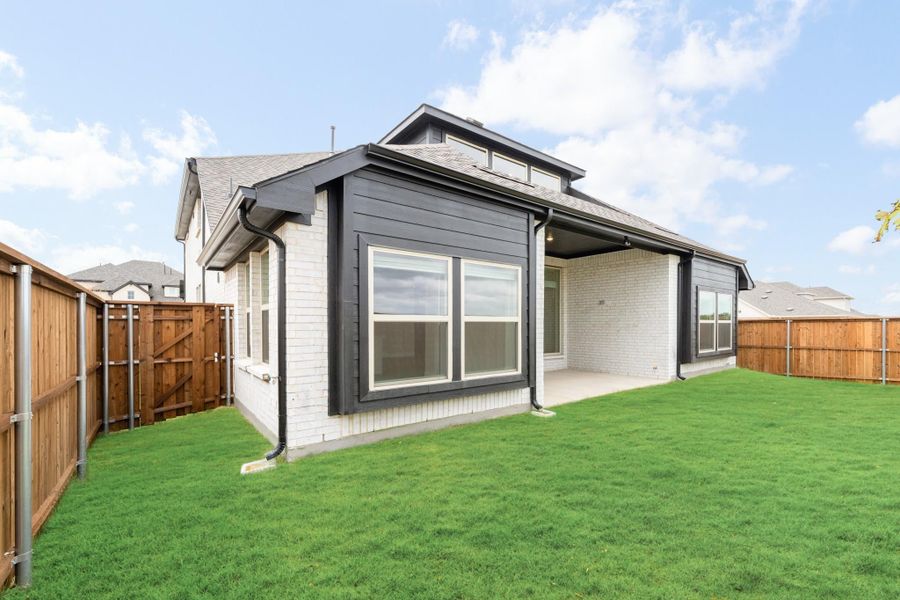 Rear exterior of home with white brick, dark trim, covered patio, and fenced backyard with green lawn