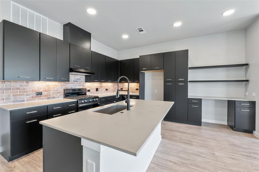 Kitchen featuring stainless steel range with gas stovetop, dark cabinetry, open shelves, light wood-style floors, and recessed lighting