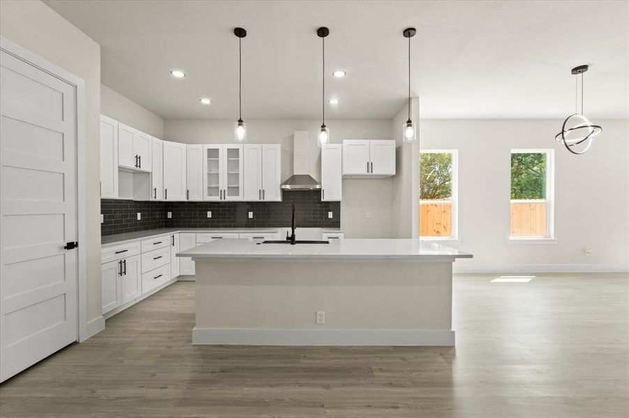 Kitchen featuring glass insert cabinets, hanging light fixtures, tasteful backsplash, white cabinetry, and a kitchen island with sink Kitchen featuring glass insert cabinets, hanging light fixtures, tasteful backsplash, white cabinetry, and a kitchen island with sink
