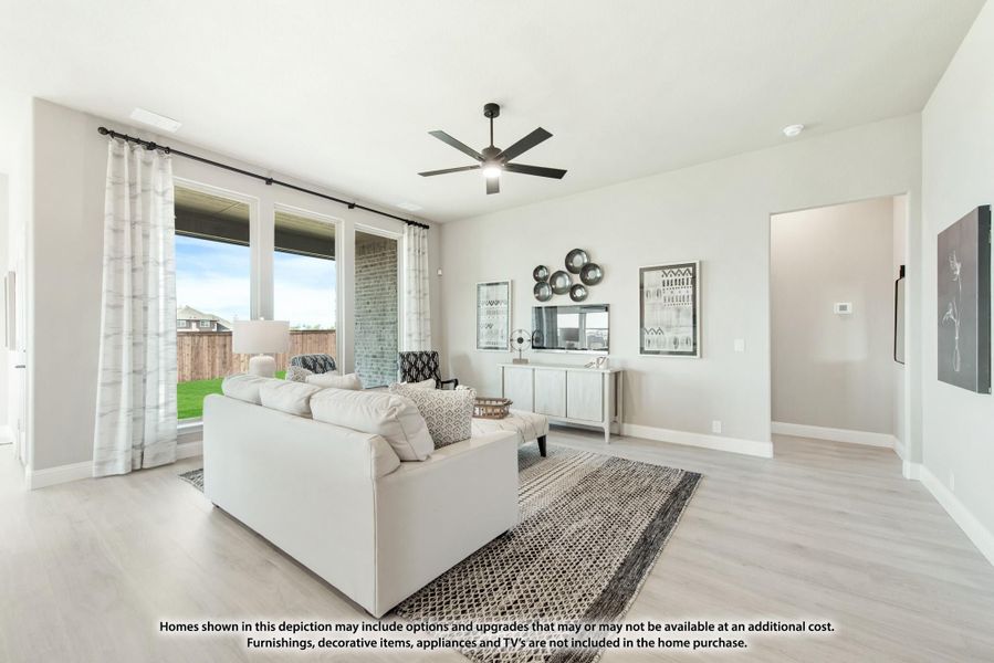 Living room with light wood floors, ceiling fan, large windows, and neutral-toned sofa and area rug Living room with light wood floors, ceiling fan, large windows, and neutral-toned sofa and area rug