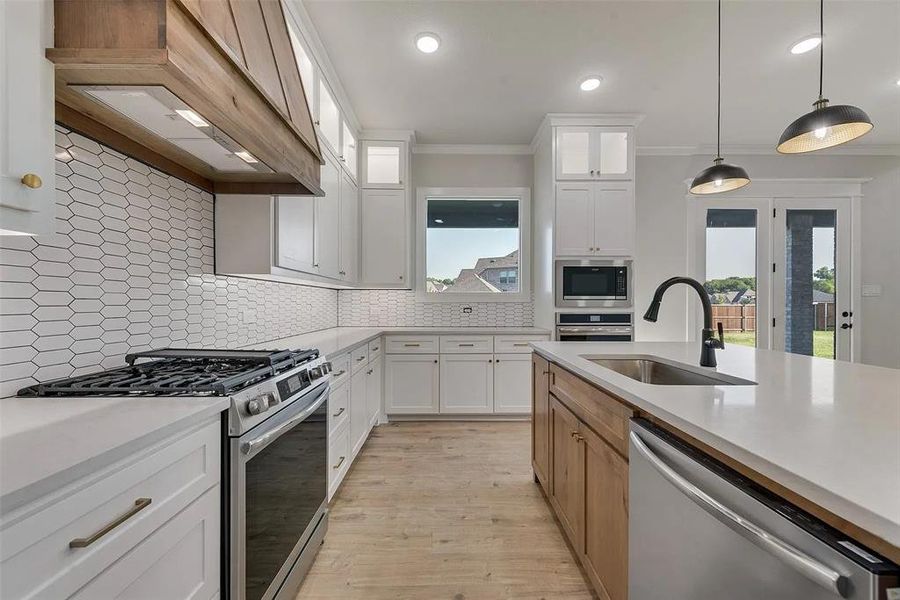 Kitchen featuring stainless steel appliances, two tone color scheme, ornamental molding, decorative light fixtures, and backsplash