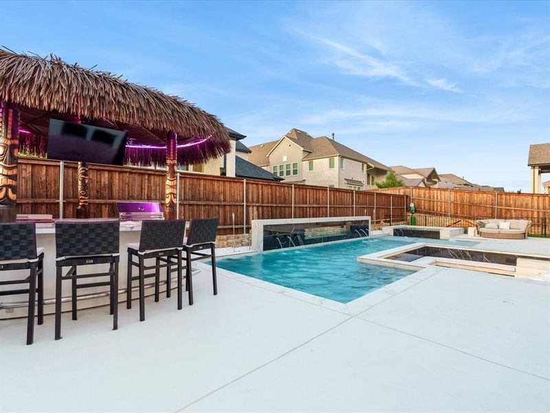 Backyard entertainment area featuring a thatched-roof bar with built-in appliances, a flat-screen television, and integrated lighting Backyard entertainment area featuring a thatched-roof bar with built-in appliances, a flat-screen television, and integrated lighting