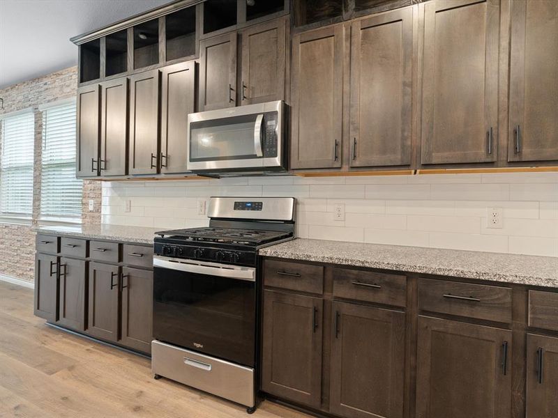 Kitchen with light stone counters, backsplash, light hardwood / wood-style flooring, and appliances with stainless steel finishes