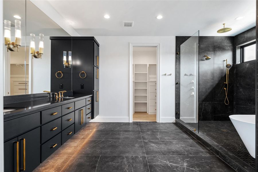 Full bathroom featuring a walk in closet, double vanity, a shower stall, a freestanding bath, and dark marble finish flooring