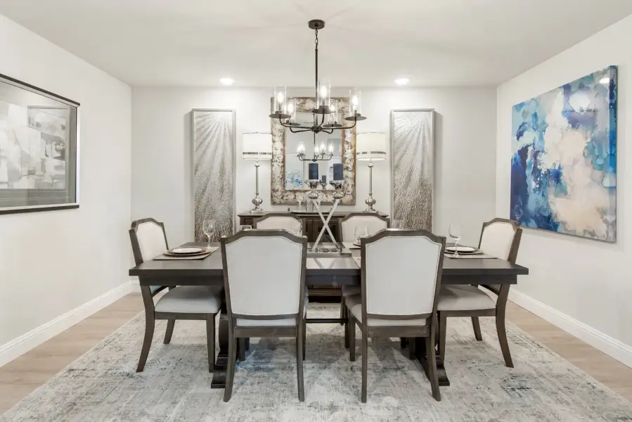 Formal dining room with dark wood table, six upholstered chairs, chandelier, and wall art on light hardwood floors